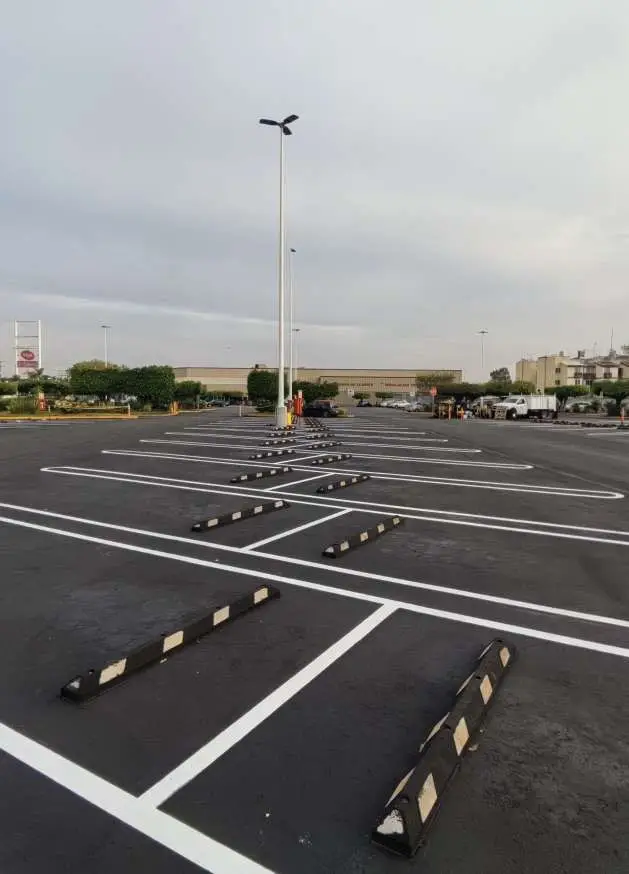 El mismo estacionamiento terminado, con el pavimento sellado, los topes colocados y las líneas de cajón pintadas.